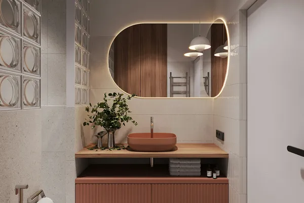 Banheiro com espelho oval iluminado, gabinete terracota e piso estampado
