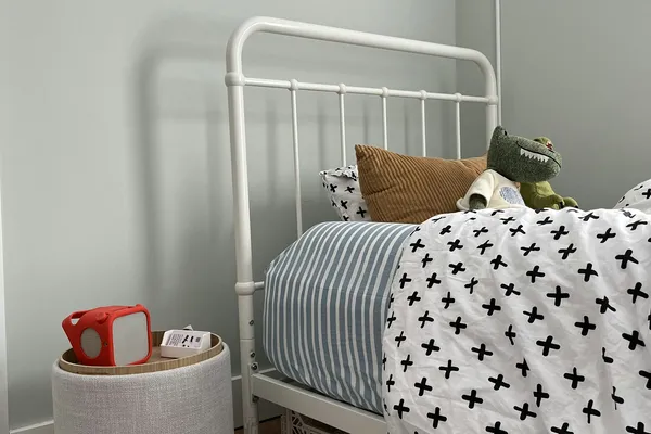 Quarto infantil com cama de ferro branca, manta estampada e tapete