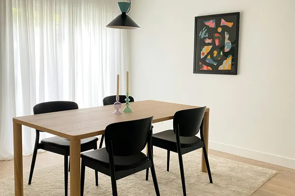 Mesa de jantar de madeira com cadeiras pretas e quadro colorido na parede