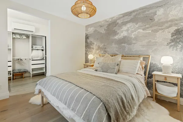 Quarto com cama de casal, roupa de cama clara e papel de parede suave