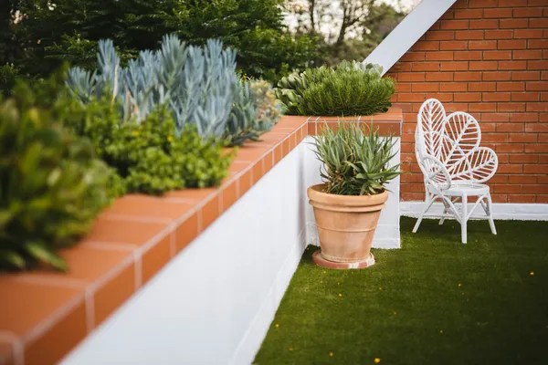Terraço com cadeira branca, vasos e grama