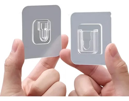 Par de mãos segurando dois ganchos adesivos transparentes quadrados para pendurar quadro sem furo, foto do anúncio do produto no Mercado Livre
